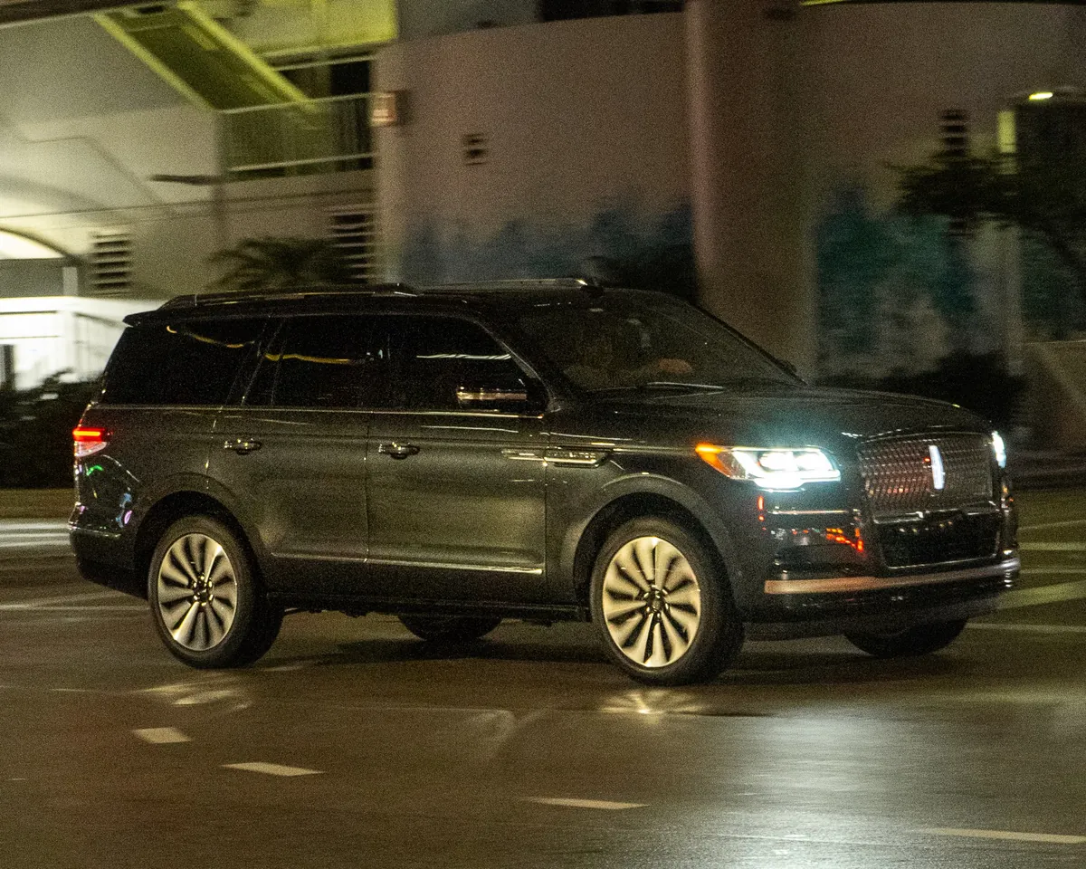 A black current-generation Lincoln Navigator at night with its headlights on