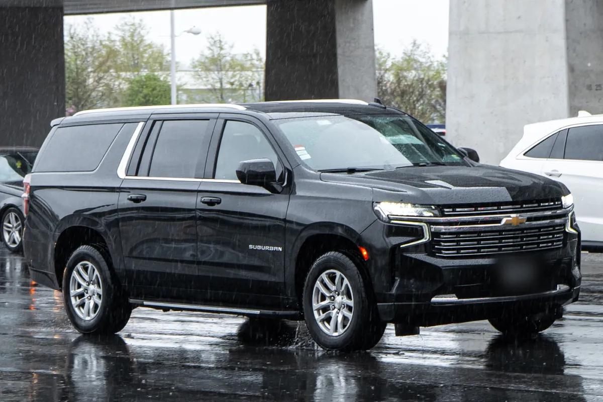 A black current-generation Chevrolet Suburban on a wet city street